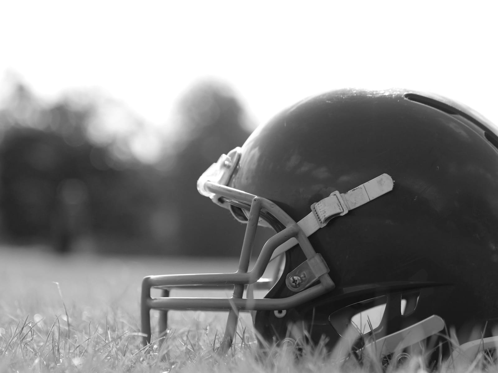 Football-Helm im Gras vor unscharfem Parkhintergrund, Gegenlicht